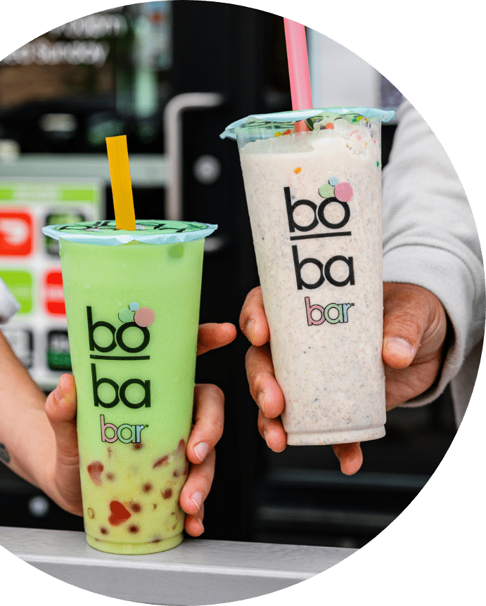 Photograph of two hands, each holding a boba tea. One boba tea is green and the other is white.